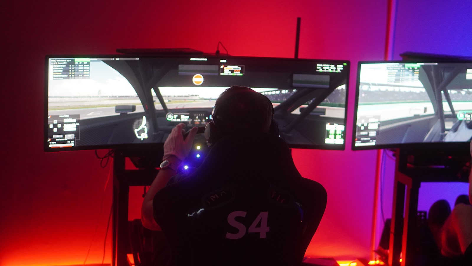 Symulator oświetlony na czerwono, na ekranach trwający wyścig